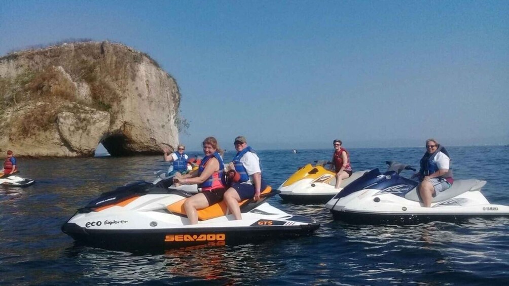 People on jet skis near a large rock formation. 4