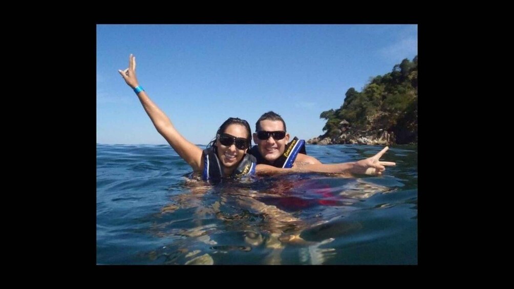 Two people snorkeling in clear blue water with rocky cliffs in the background. 1