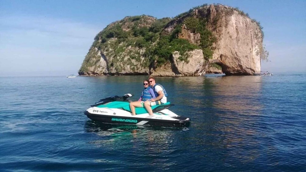 Two people on a jet ski in calm waters with a large rock formation in the background. 5