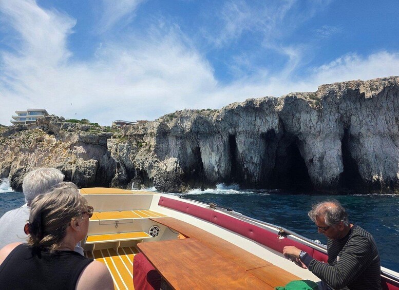 A boat with passengers, rocky cliffs, and a building in the background. 2
