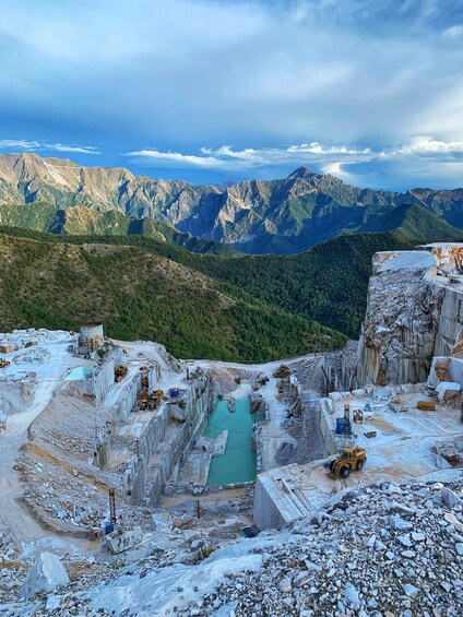 A quarry with a turquoise pool surrounded by rocky terrain and mountains in the background. 2