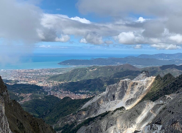 A mountainous landscape with a winding road, a coastal city in the distance, and a clear sky with clouds. 3