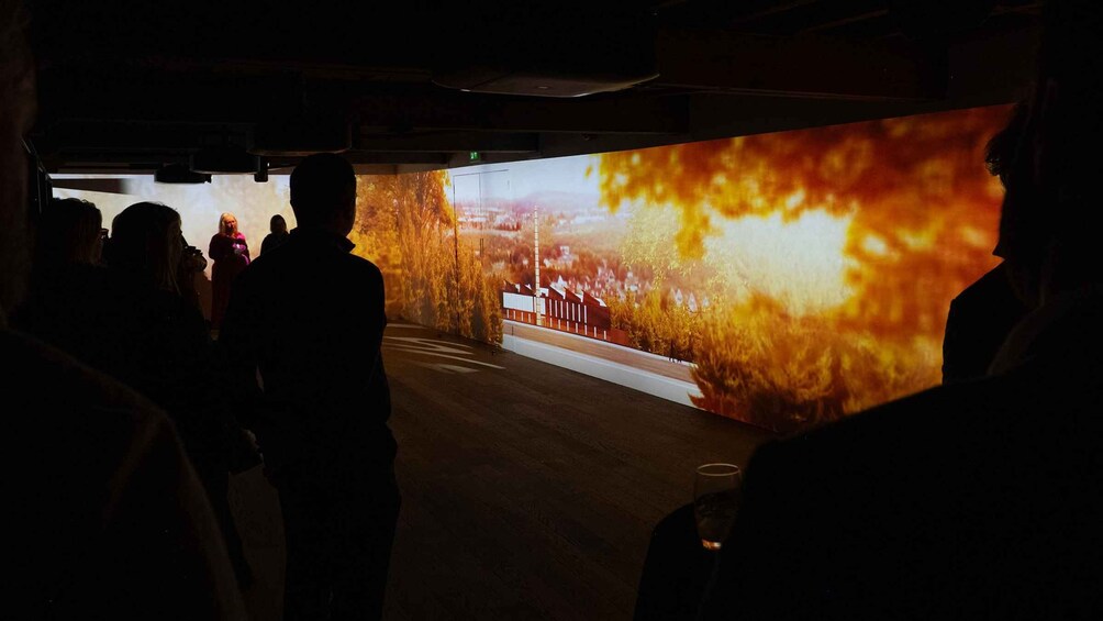 A group of people walking in a dimly lit corridor with a large digital display on the right side. 5