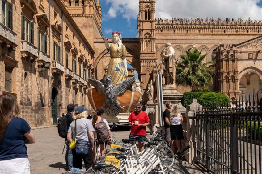 A historic plaza with a large statue, tourists, and bicycles. 4