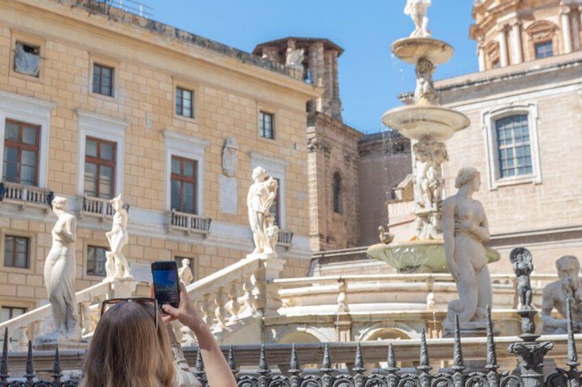 A person taking a photo of a fountain with statues in an urban setting. 5