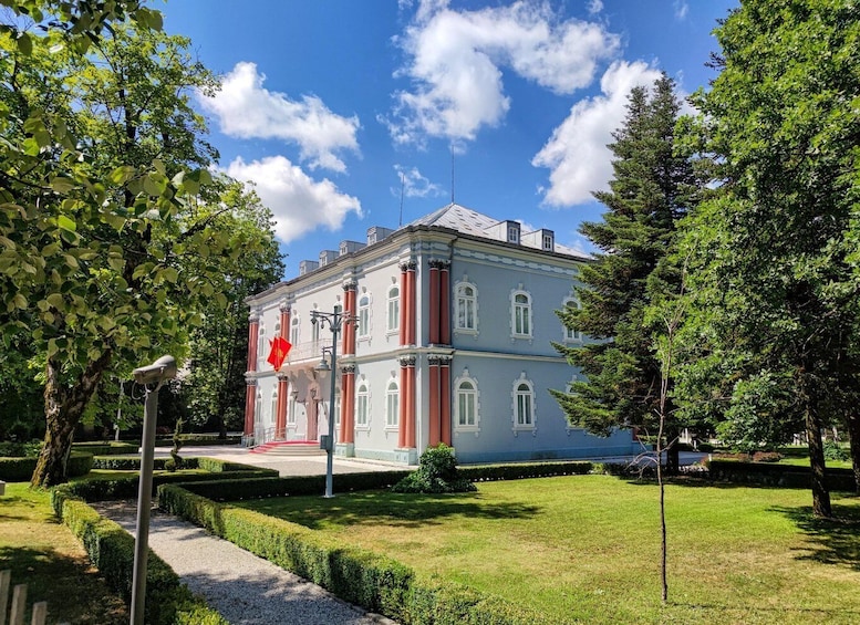 A classical building with a red flag, surrounded by well-maintained hedges and trees. 1