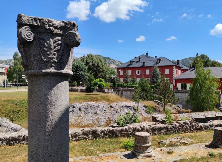 A stone column with carvings, a red building, and a mountainous landscape in the background. 2