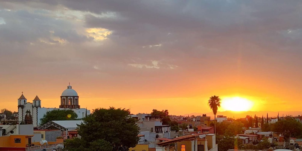 A sunset over a cityscape with a prominent church and palm trees. 1