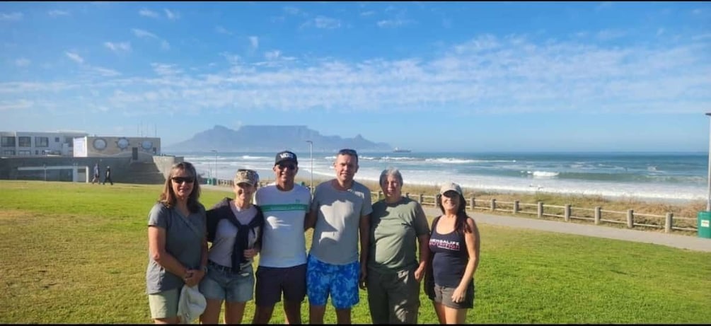 A group of people standing on a grassy area near a beach with a view of the ocean and a mountain in the distance. 4