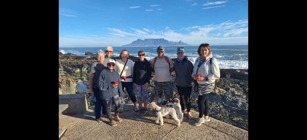 A group of people standing on a rocky outcrop with a view of the ocean and distant mountains. 5