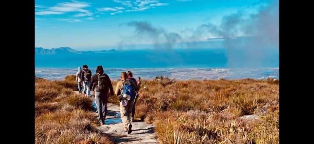 A group of people hiking on a trail with a view of a coastal landscape. 1