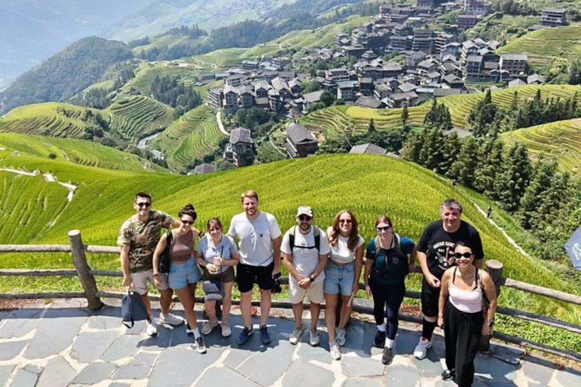 A group of people standing on a stone pathway with a scenic view of terraced vineyards and a village in the background. 1