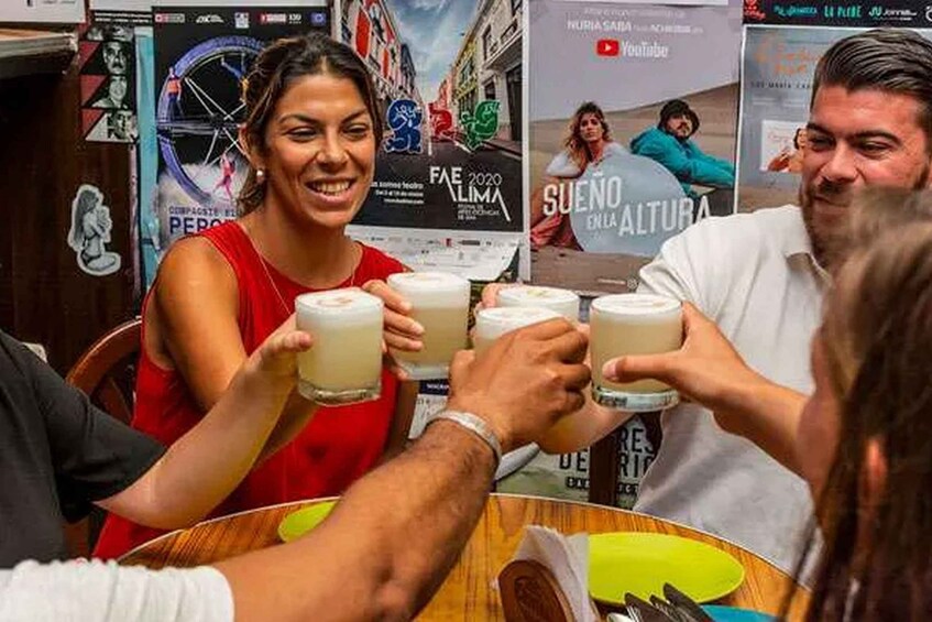 People toasting with drinks at a table with posters in the background. 2