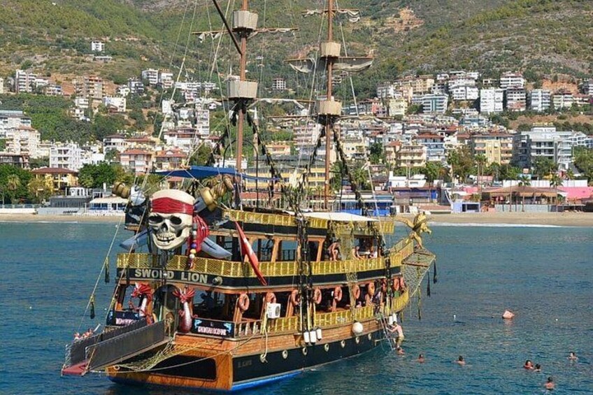 A pirate-themed boat named 'SWOOP LION' with a skull and crossbones, sailing on water with a coastal town in the background. 1