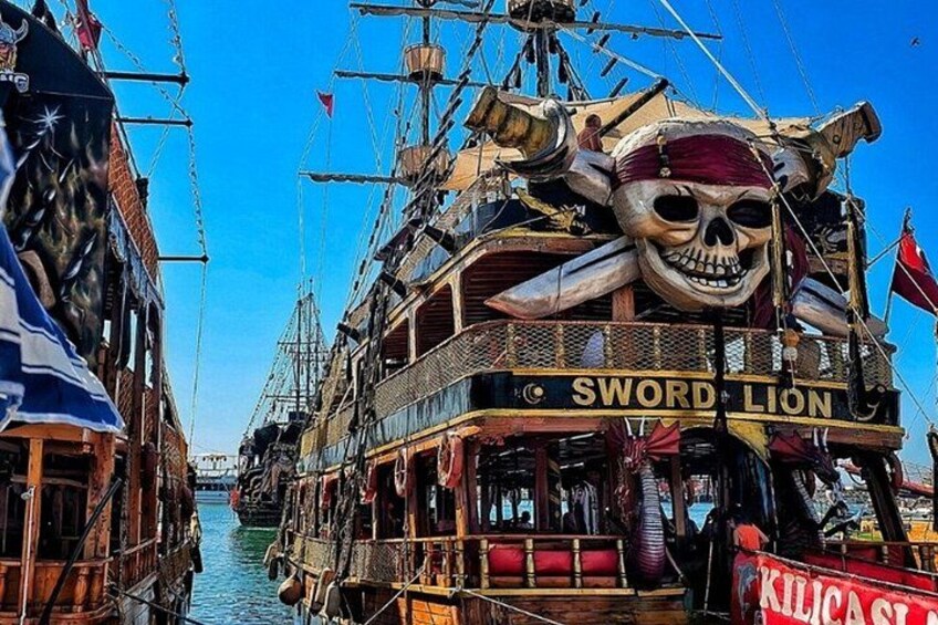 A large ship named 'Sword Lion' with a skull decoration, docked at a harbor with other ships. 3