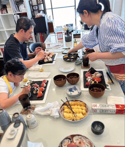 A group of people dining at a table with various dishes of sushi and other foods. 1