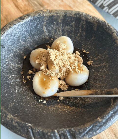 A bowl containing three round, white objects with a brown topping, placed on a dark surface. 2