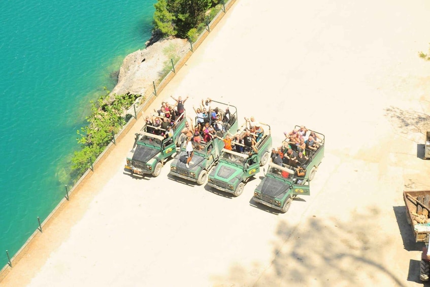 A group of people in green safari vehicles parked on a beach by the sea. 3