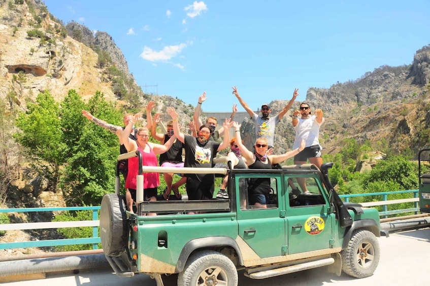 A group of people celebrating on a green off-road vehicle with a rocky landscape in the background. 1
