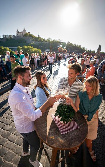 A group of people toasting with drinks at a round wooden table with a checkered napkin and a potted plant. 3