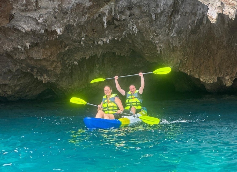 Two people kayaking in clear blue water with a cave in the background. 2
