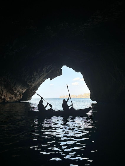 Two people kayaking in a cave opening with a view of the sea and distant land. 3