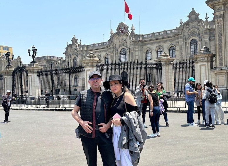 A couple standing in front of a grand building with ornate architecture and a red flag. 4