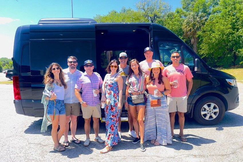 A group of people standing in front of a black van in a parking lot. 2