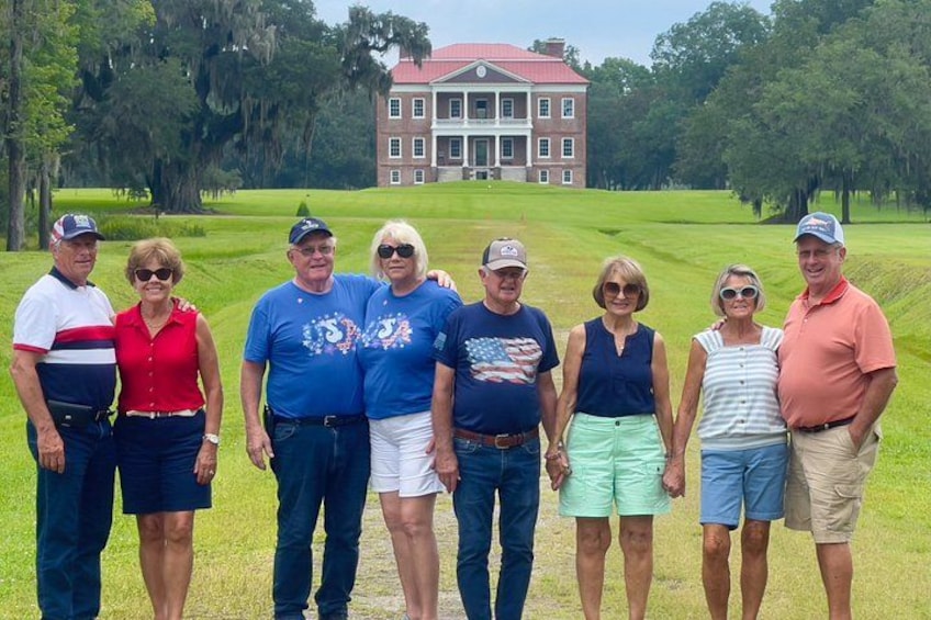 A group of people standing on a golf course with a large house in the background. 1