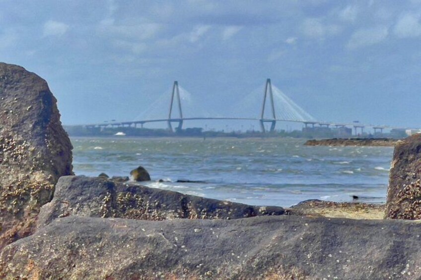 A coastal landscape with large rocks in the foreground and a bridge in the background. 3