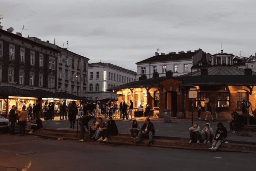 A bustling evening street scene with people walking and sitting, surrounded by historic buildings with illuminated facades. 2
