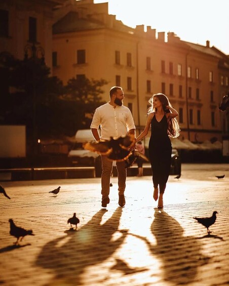 Un couple se promène, main dans la main, sur une rue pavée, avec des pigeons et des bâtiments en arrière-plan. 5