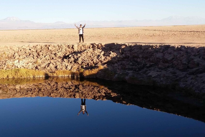 Una persona de pie sobre una cornisa rocosa sobre aguas tranquilas, con montañas al fondo. 2