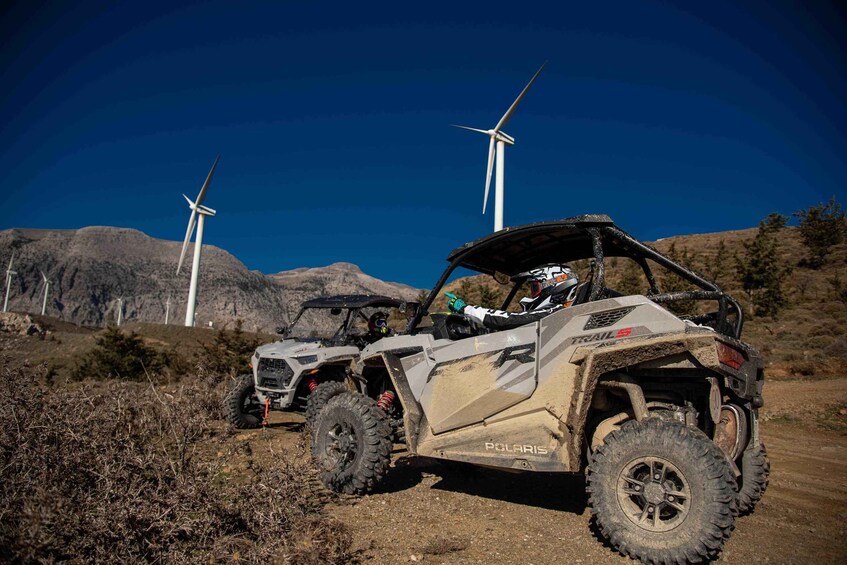 Two Polaris off-road vehicles on a dirt path with wind turbines in the background. 4