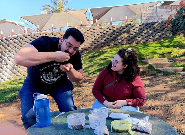 Two people sitting at a table outdoors with food items and a blue water bottle. 3