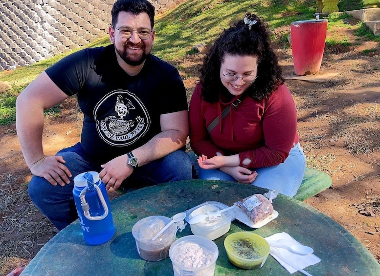Two people sitting on a green surface outdoors with food items and a blue water bottle. 2