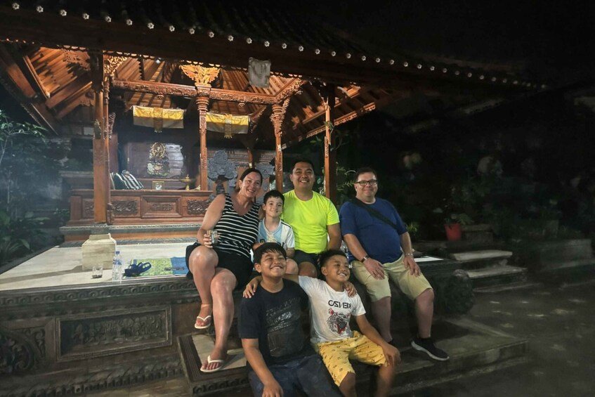 A group of people seated on stone steps under a wooden pavilion with intricate carvings. 2