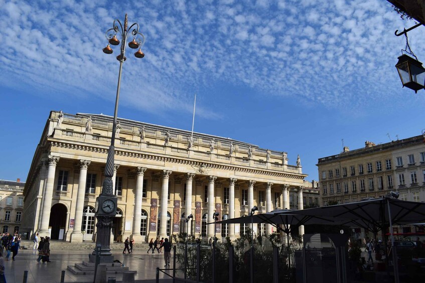 A historic building with columns and a clock, surrounded by people and a covered area. 2