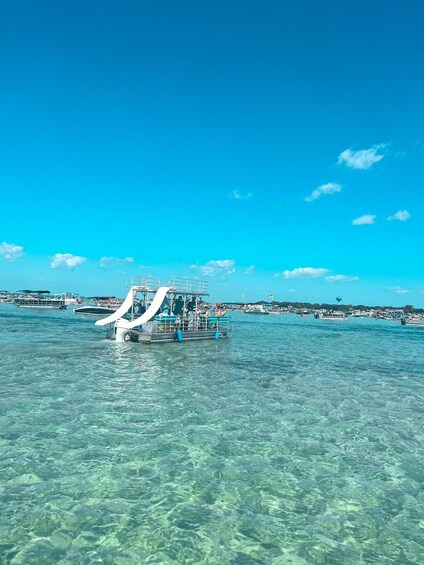 A clear blue sea with a boat in the foreground and several other boats in the background. 4