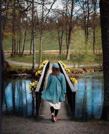 A person walking on a wooden bridge over a body of water, surrounded by trees and yellow flowers. 3