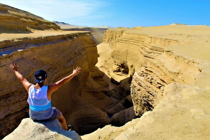 A person sitting on a rock with arms outstretched in a canyon. 1