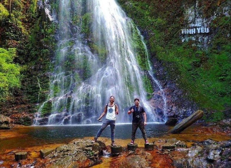 Two people standing on rocks in front of a waterfall. 2