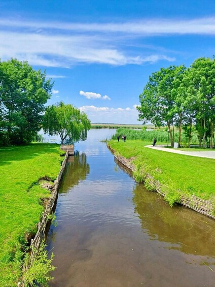 A calm river with a wooden walkway on one side and a grassy area with trees on the other. 2