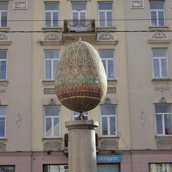 Un huevo decorativo sobre una columna frente a un edificio con múltiples ventanas y un letrero que dice "Drogas". 4