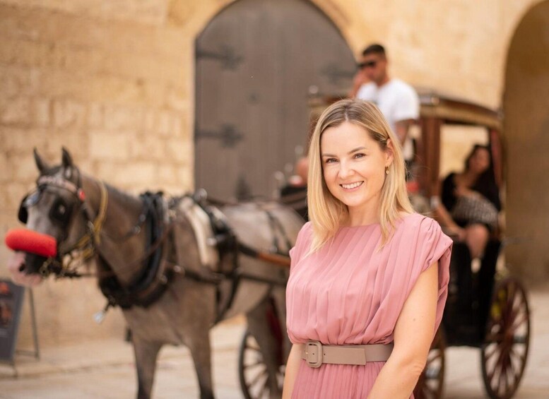 A woman in a pink dress standing in front of a horse-drawn carriage. 1