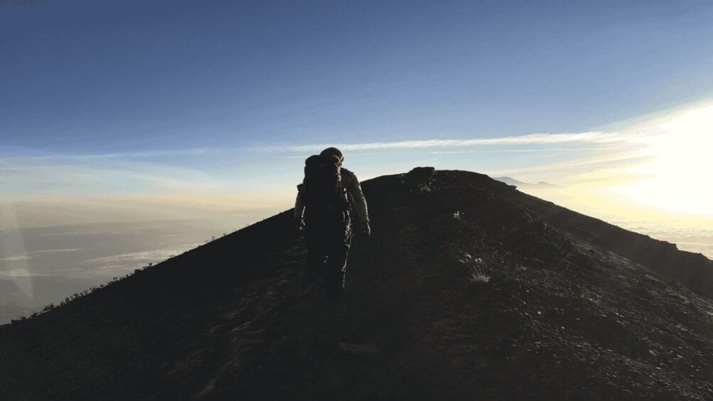 A person hiking on a mountain trail with a view of the ocean in the background. 1