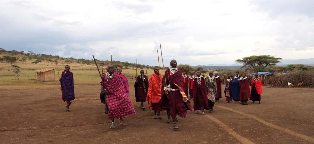 A group of people in traditional attire walking across a dry, open landscape with sparse vegetation and a few trees in the background. 1