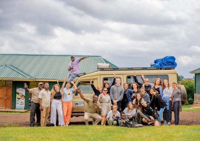 A group of people posing in front of a van and a building with a green roof. 2