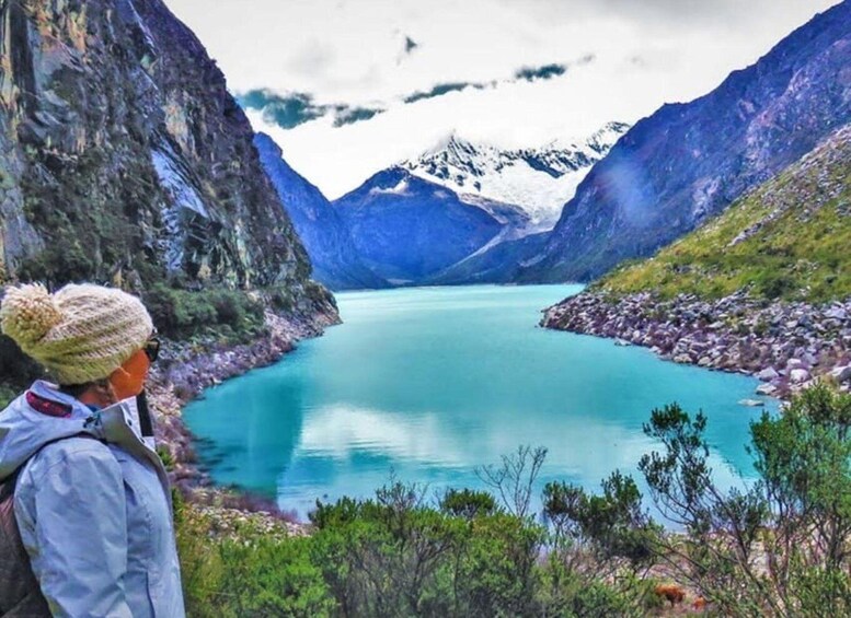 A person standing by a turquoise lake surrounded by mountains. 1