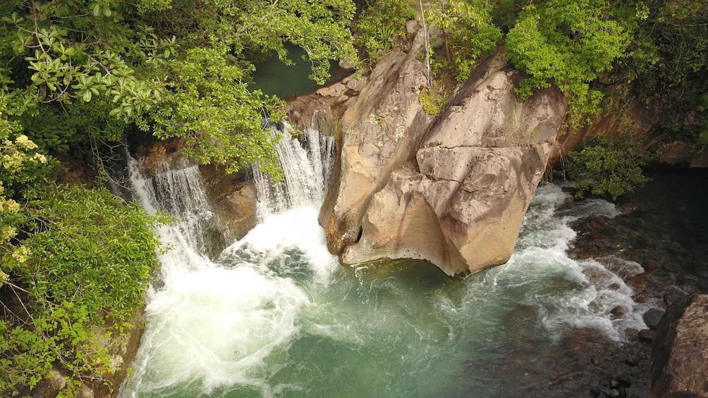 A waterfall cascading over a rocky cliff surrounded by lush greenery. 1
